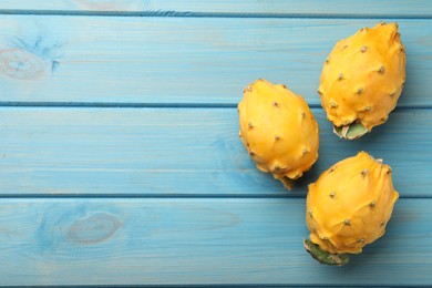 Photo of Delicious yellow pitahaya fruits on light blue wooden table, flat lay. Space for text