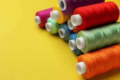 Photo of Different colorful sewing threads on yellow background, closeup. Space for text