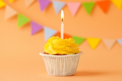 Photo of Tasty birthday cupcake with candle on orange table against party flags