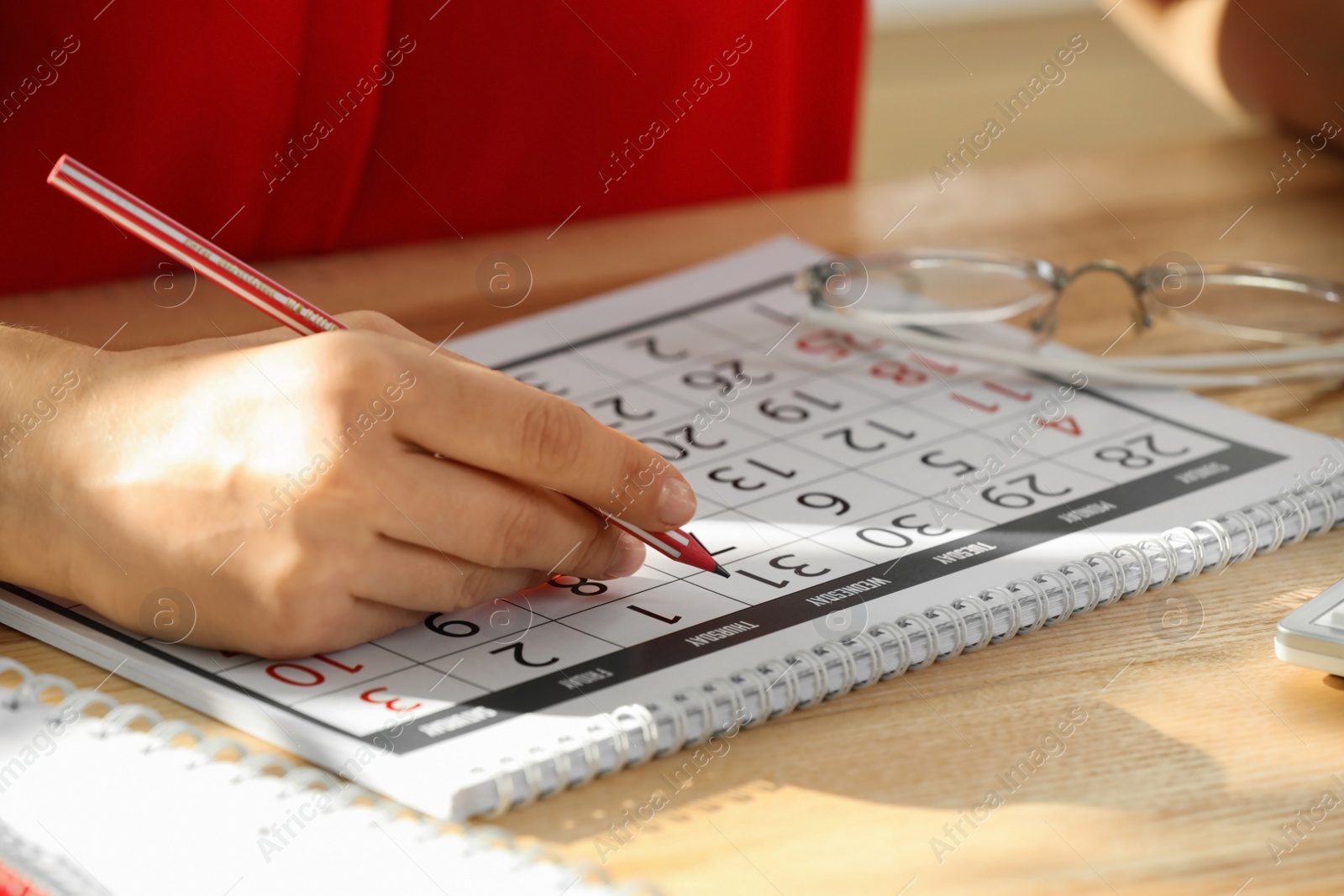 Photo of Woman marking date in calendar at wooden table, closeup