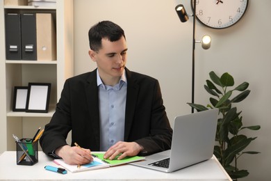 Photo of Man taking notes at table in office