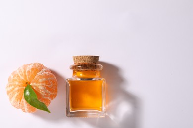 Photo of Aromatic tangerine essential oil in bottle and citrus fruit on white table, top view. Space for text