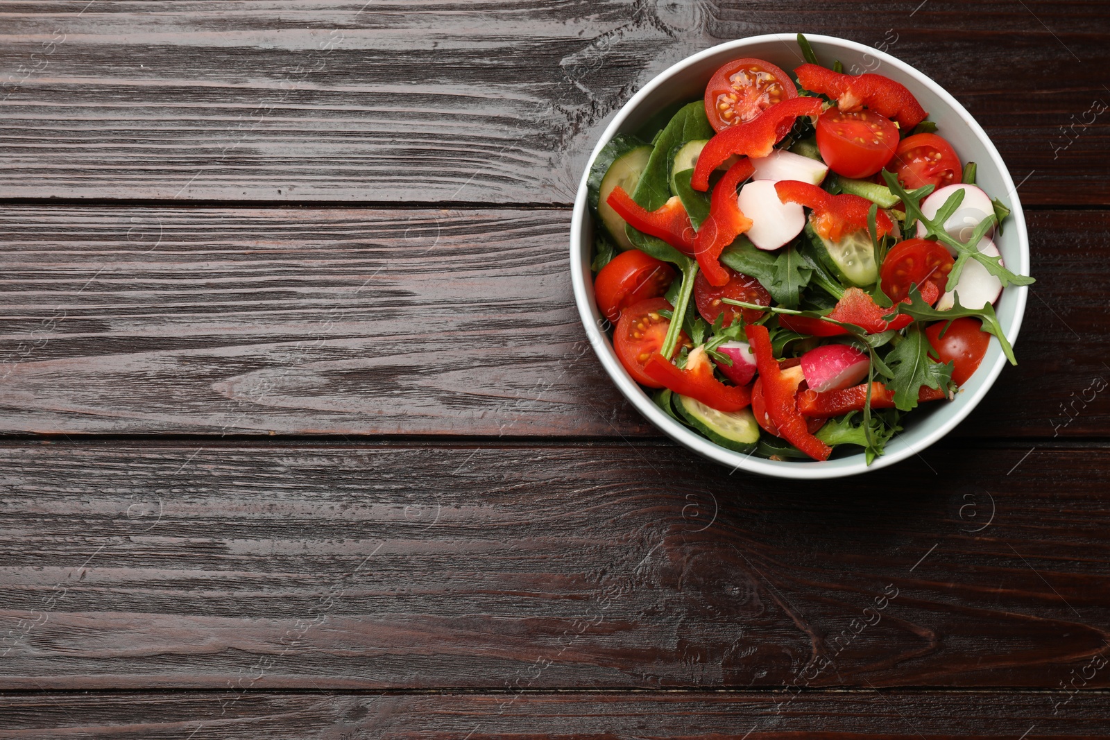 Photo of Tasty fresh vegetarian salad on dark wooden table, top view. Space for text