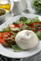 Photo of Delicious burrata salad with tomatoes, arugula and pesto sauce served on white marble table, closeup