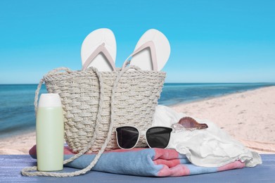 Image of Stylish bag and other beach accessories on blue wooden table near sea