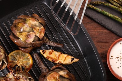 Photo of Tasty grilled artichokes on wooden table, flat lay