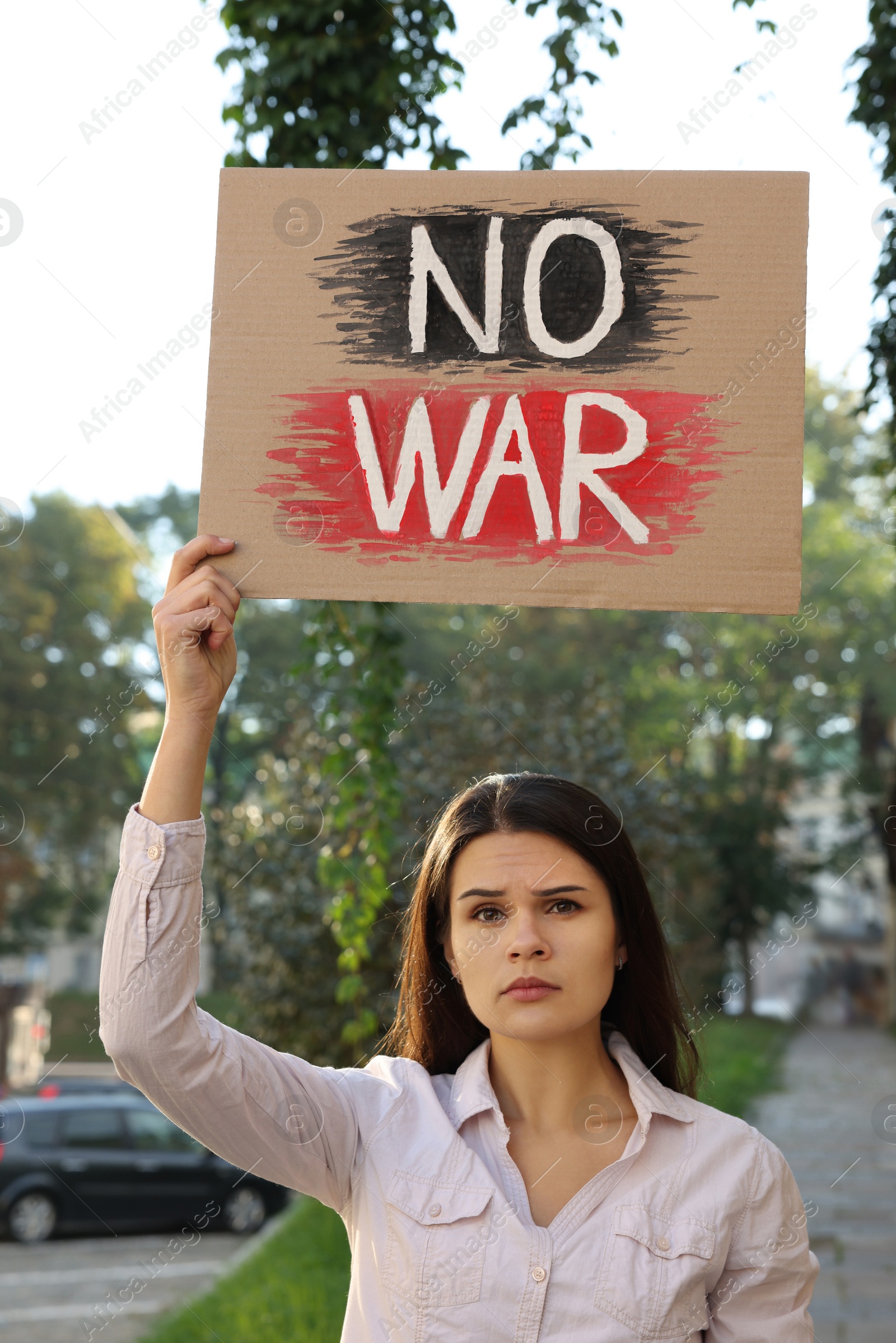 Photo of Sad woman holding poster with words No War on city street