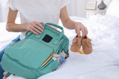 Photo of Woman packing baby accessories into maternity backpack on bed, closeup
