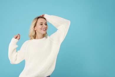 Happy woman in stylish warm sweater on light blue background. Space for text