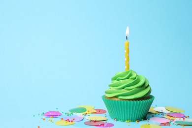 Photo of Delicious birthday cupcake with green cream and burning candle on light blue background. Space for text