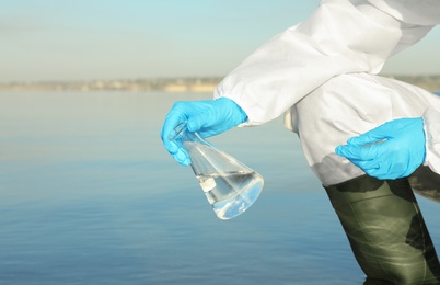 Photo of Scientist with conical flask taking sample from river for analysis, closeup