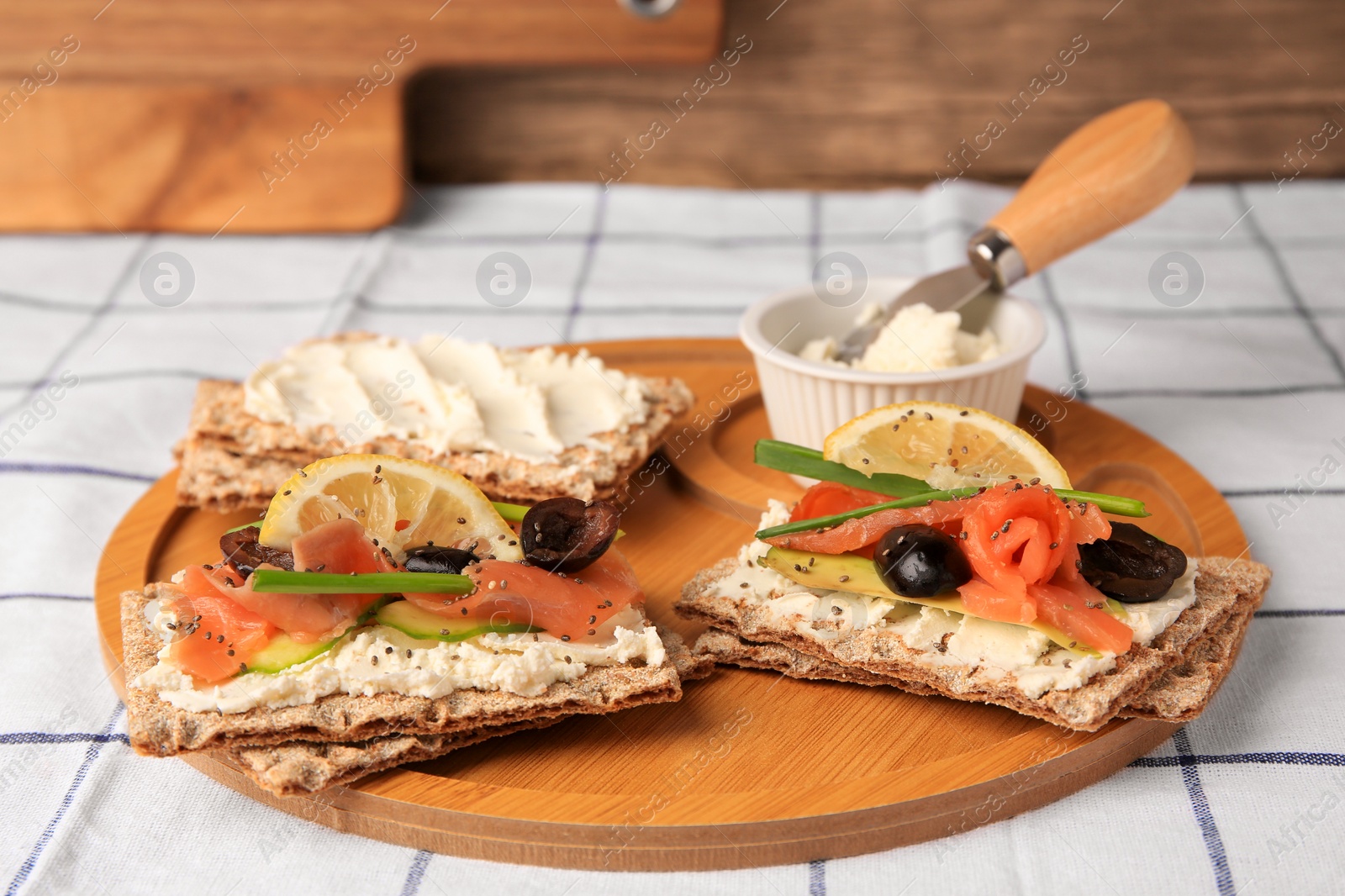 Photo of Fresh crunchy crispbreads with cream cheese, salmon, olives, lemon and green onion on table