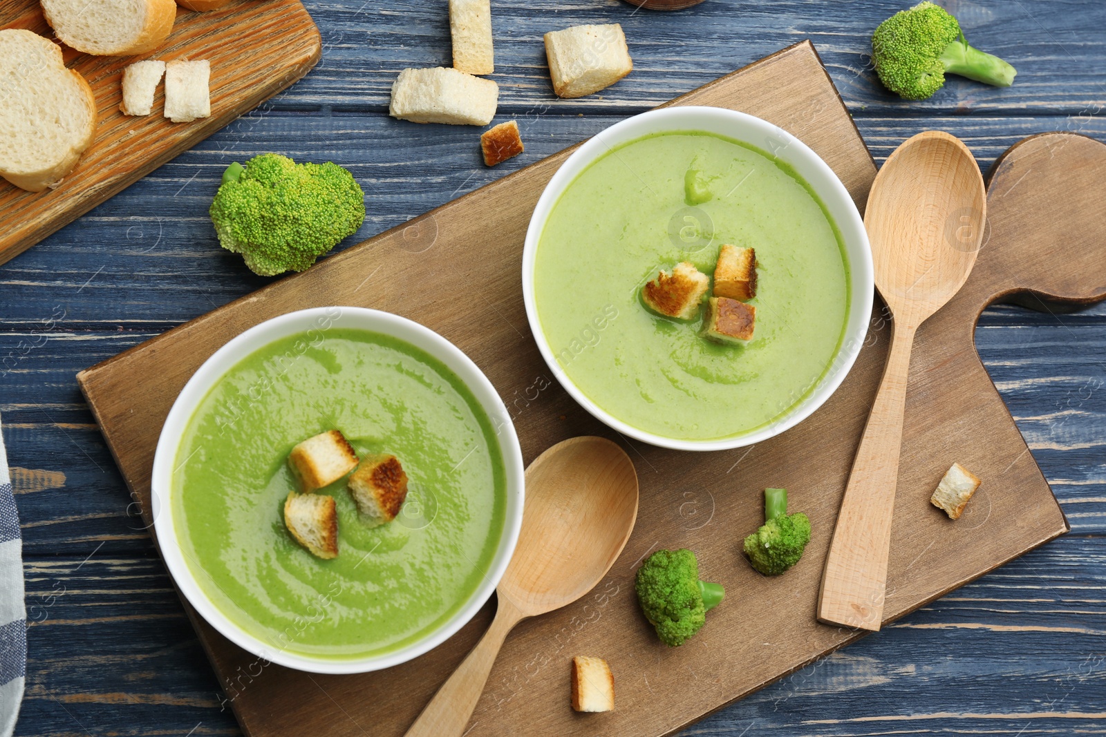 Photo of Flat lay composition with bowls of broccoli cream soup on blue wooden table