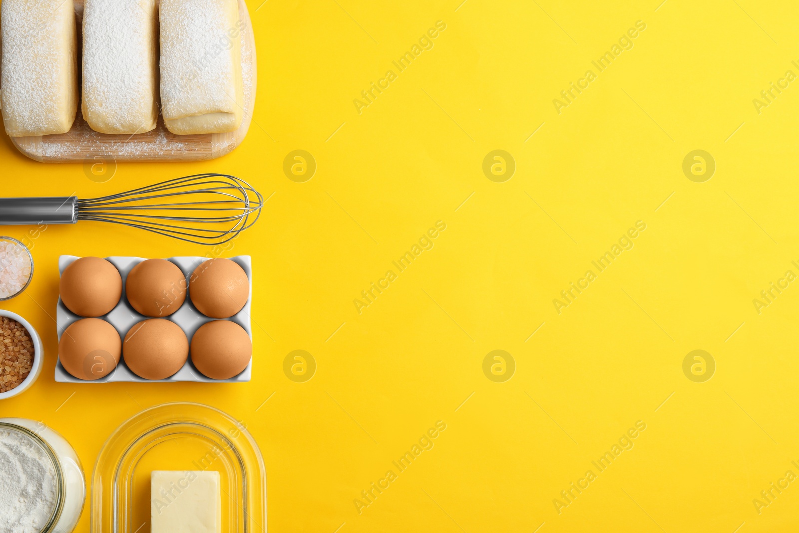 Photo of Puff pastry dough and ingredients on yellow background, flat lay. Space for text