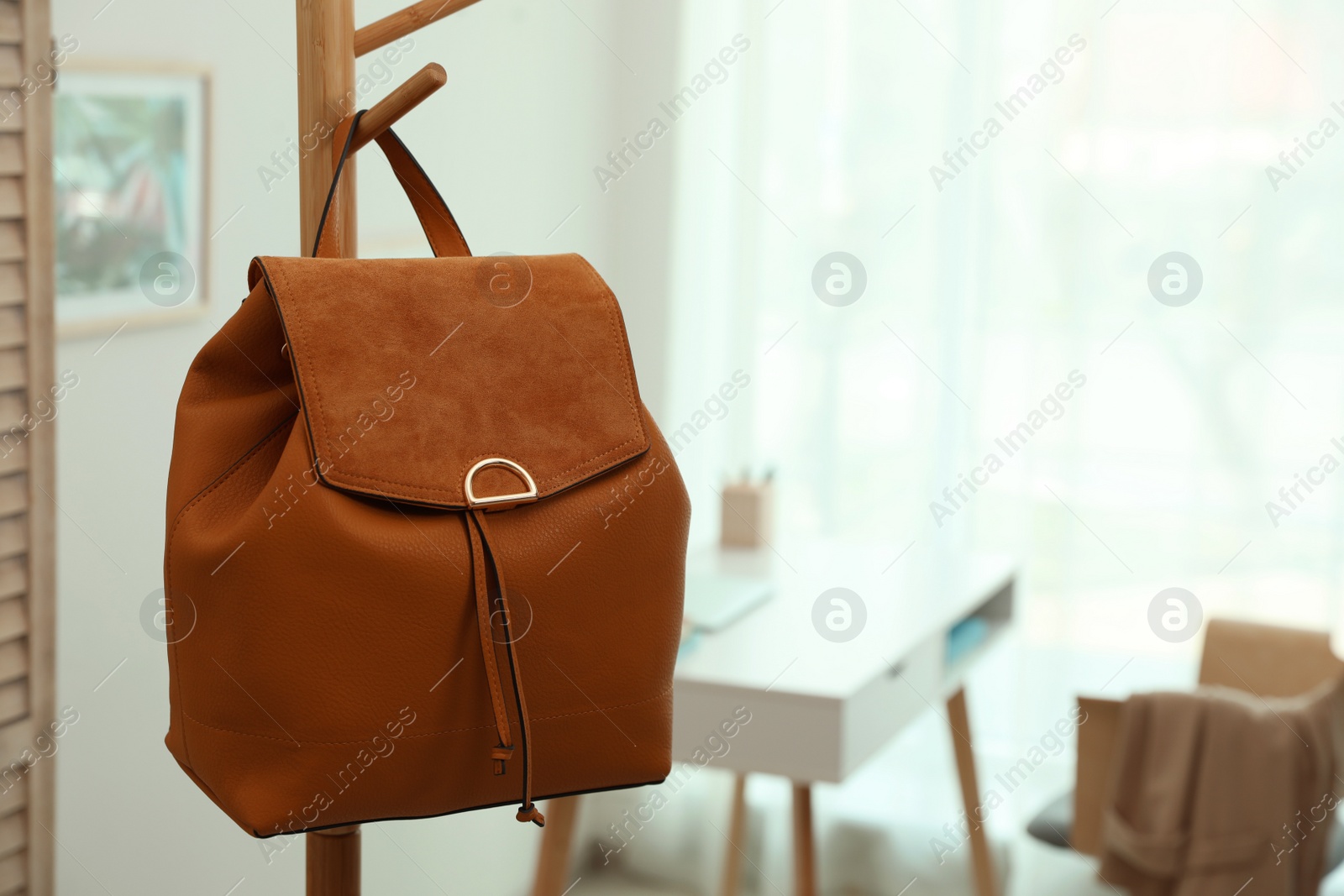 Photo of Stylish urban backpack on clothes rack in room. Space for text