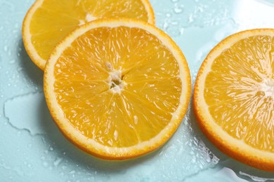 Slices of juicy orange and water on light blue background, closeup