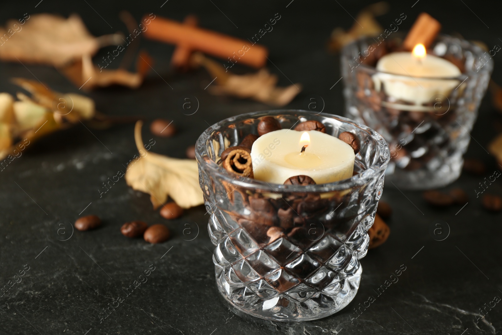 Photo of Glass holders with burning candles, coffee beans and cinnamon on black stone table, closeup