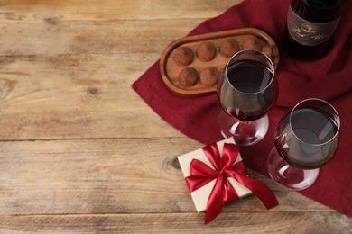 Photo of Red wine, chocolate truffles and gift box on wooden table, flat lay. Space for text