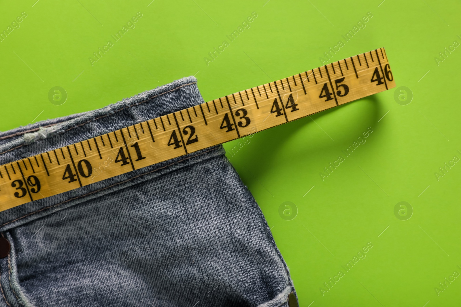 Photo of Jeans with measuring tape on green background, top view. Weight loss concept