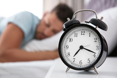 Man sleeping at home in morning, focus on alarm clock. Space for text