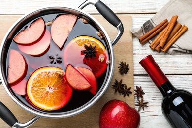 Delicious mulled wine and ingredients on white wooden table, flat lay