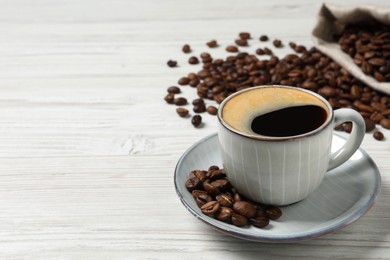 Cup of aromatic hot coffee and beans on white wooden table, space for text