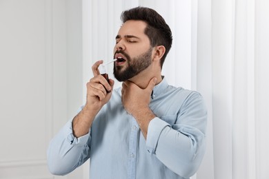 Photo of Young man using throat spray at home