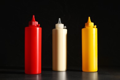 Photo of Ketchup, mustard and mayonnaise in squeeze bottles on grey table