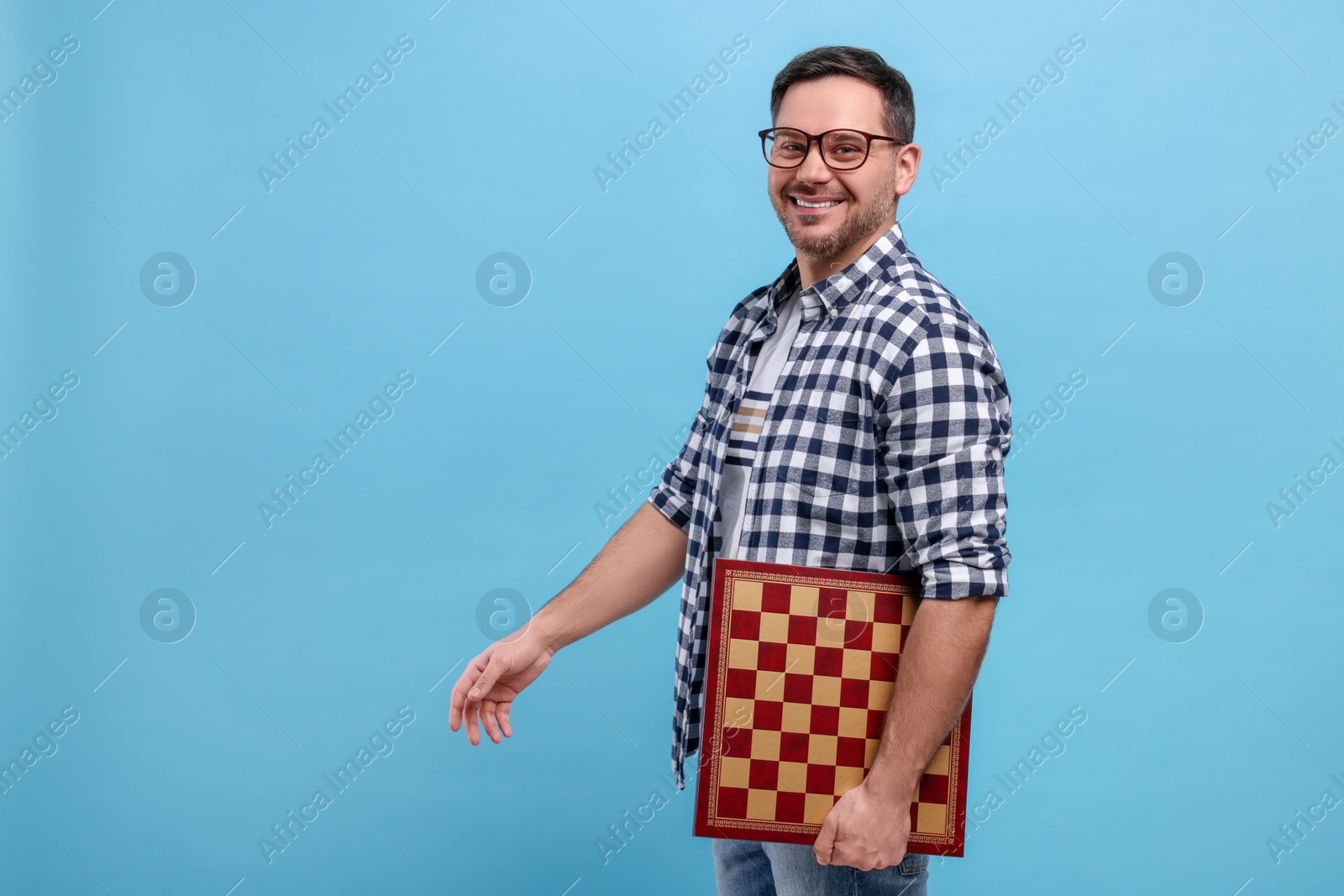 Photo of Smiling man holding chessboard on light blue background, space for text