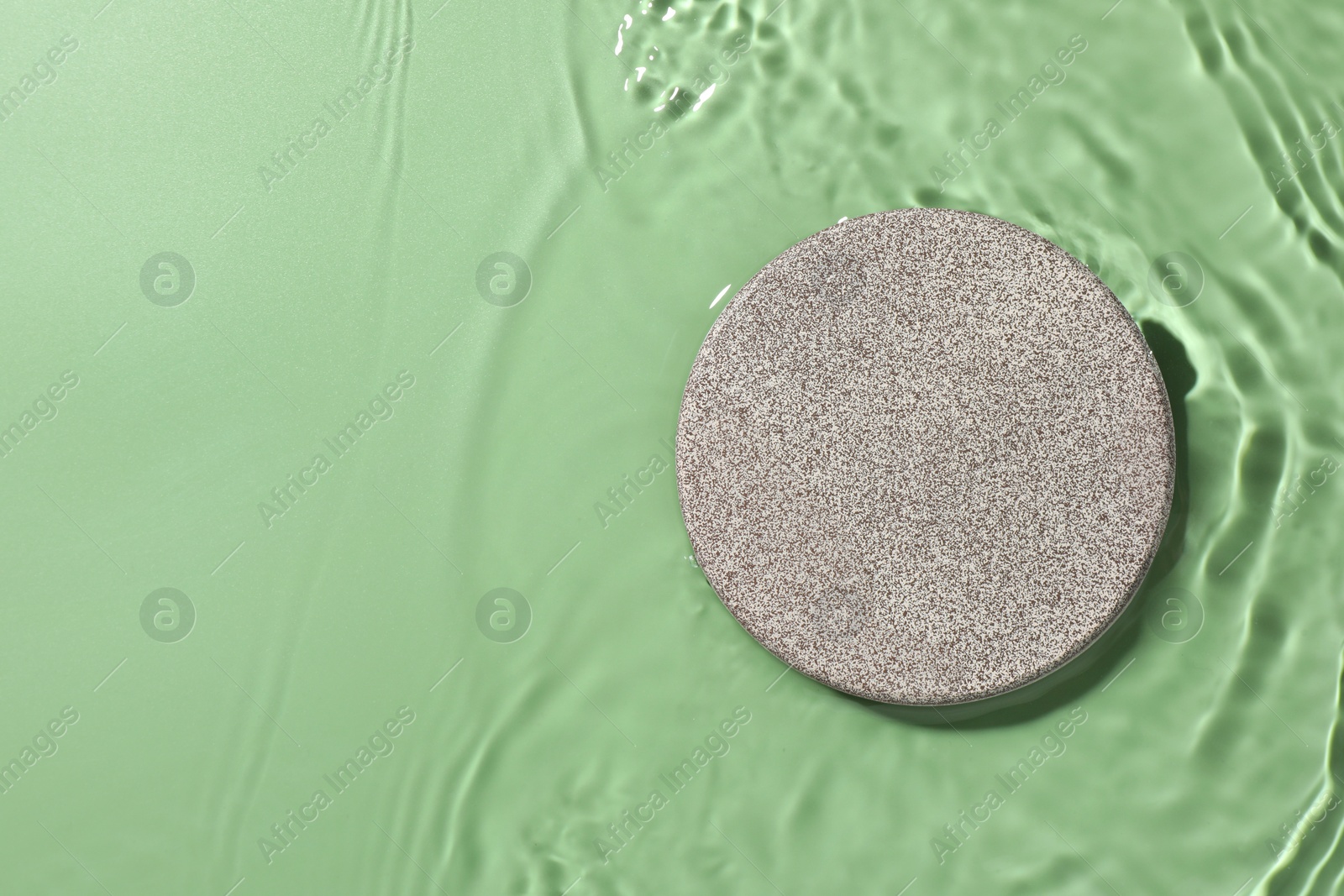 Photo of Presentation of product. Stone podium in water on green background, top view. Space for text