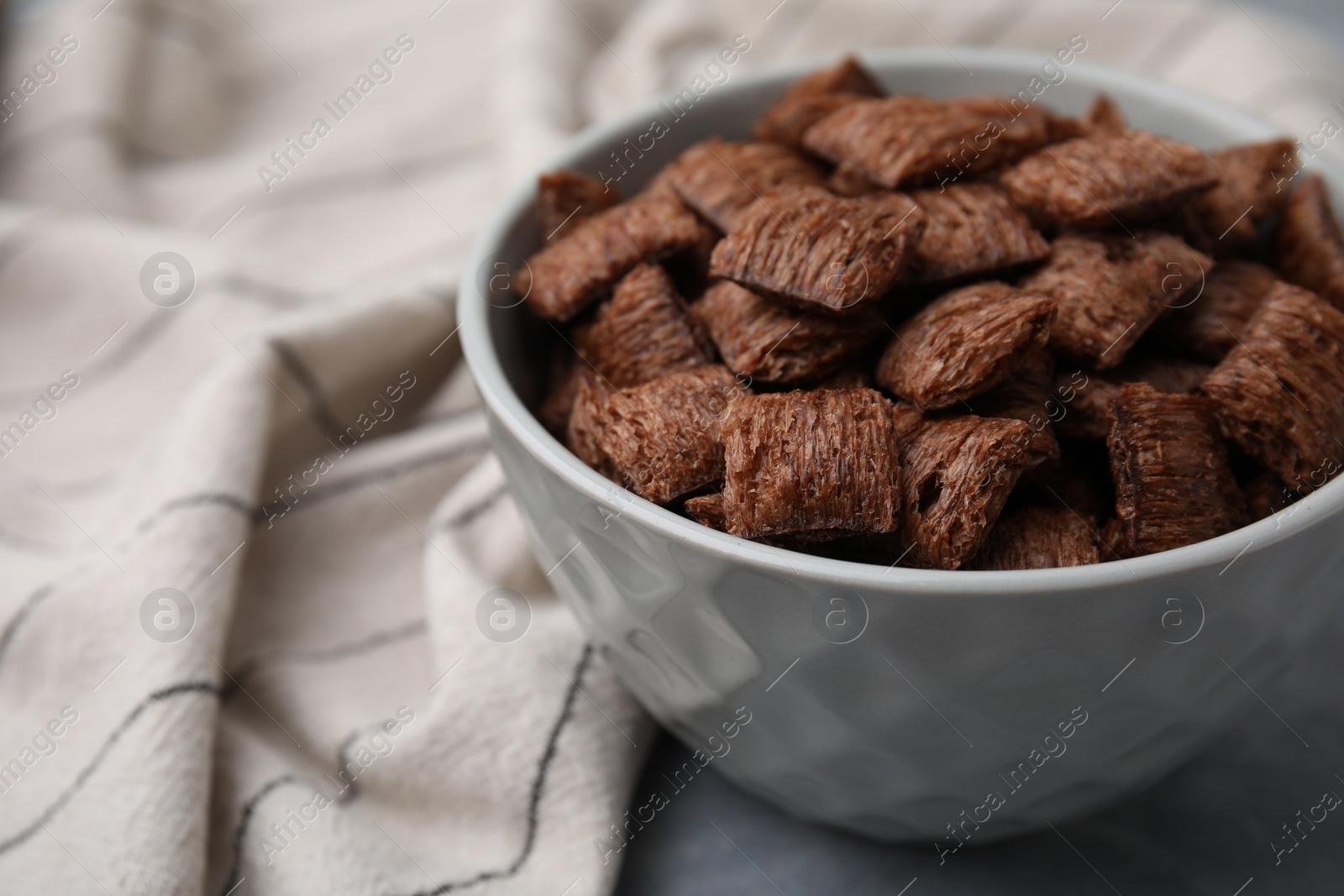 Photo of Chocolate cereal pads in bowl on grey table, closeup. Space for text