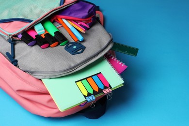 Photo of Backpack with school stationery on light blue background. Space for text