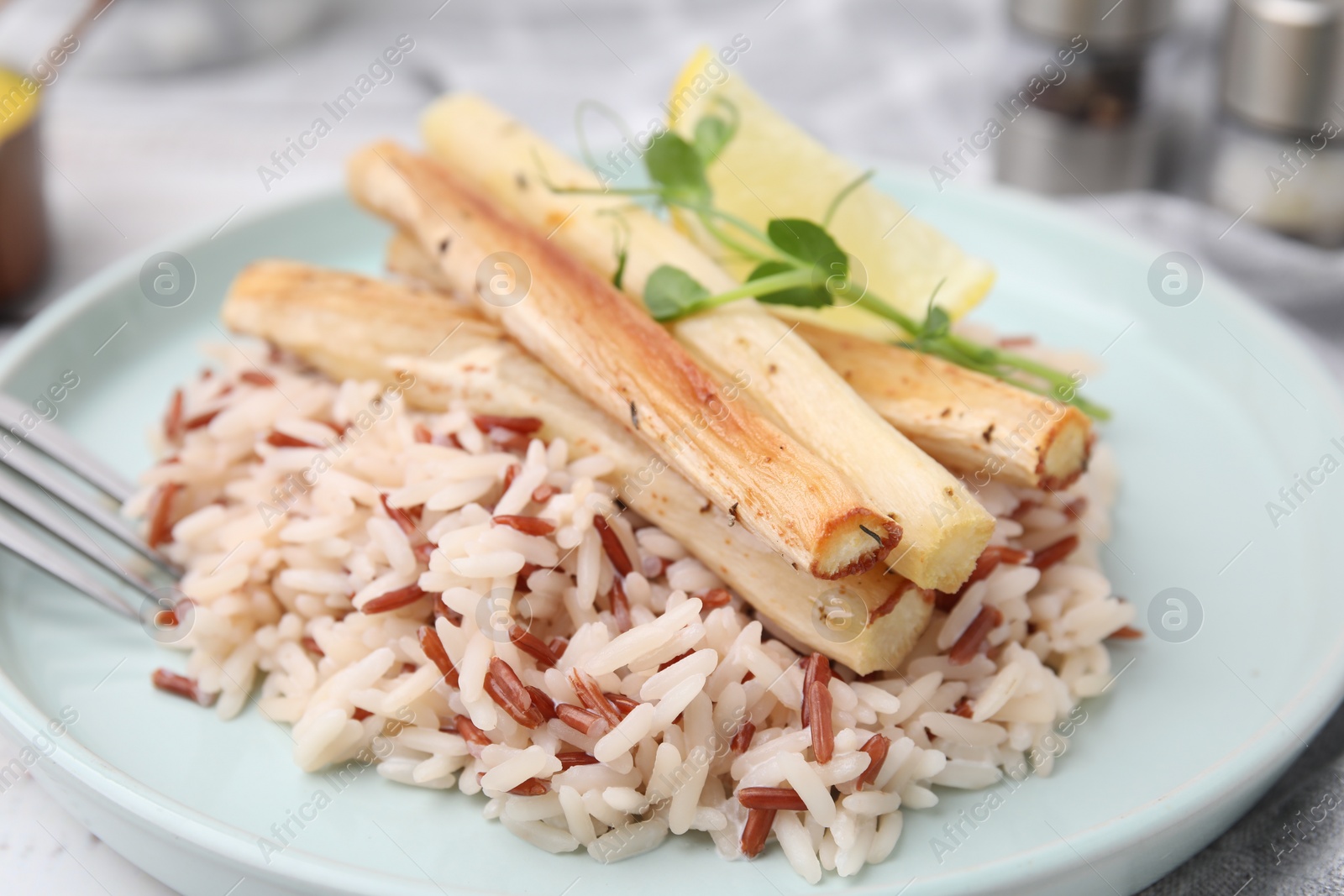 Photo of Plate with baked salsify roots, lemon and rice on table, closeup