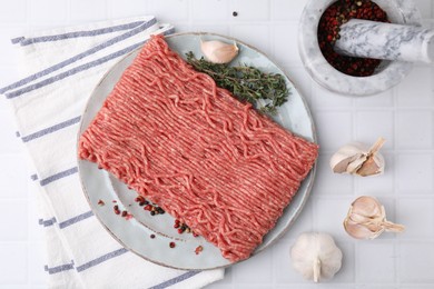 Photo of Fresh raw ground meat, peppercorns, garlic and thyme on white tiled table, flat lay