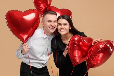 Photo of Lovely couple with heart shaped balloons on beige background. Valentine's day celebration