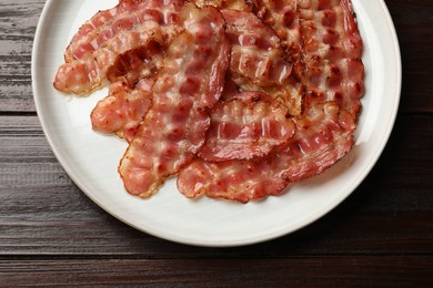 Plate with fried bacon slices on wooden table, top view