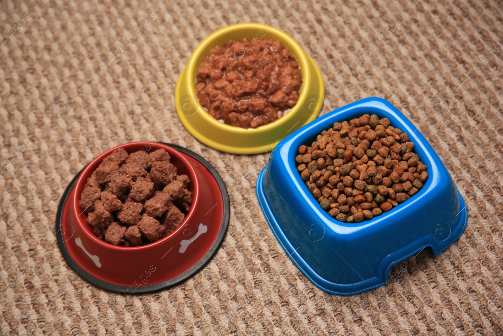 Photo of Dry and wet pet food in feeding bowls on soft carpet, above view