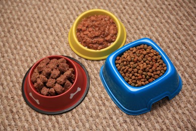 Photo of Dry and wet pet food in feeding bowls on soft carpet, above view