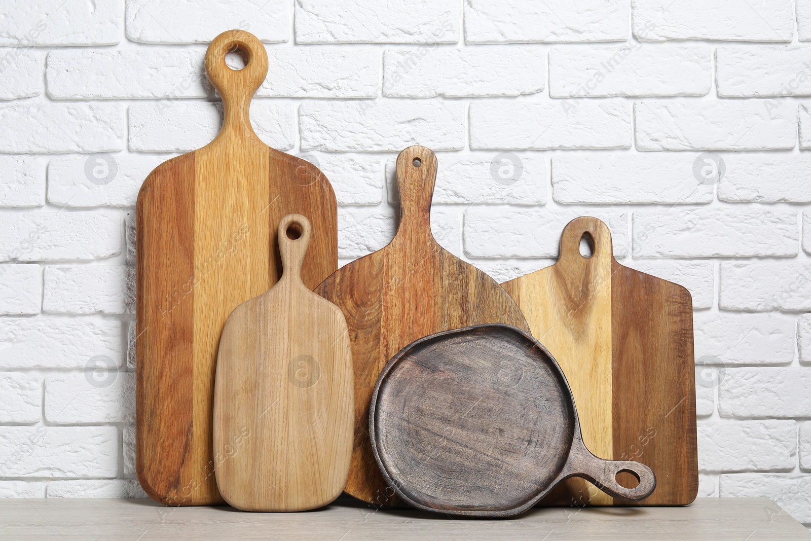 Photo of Different wooden cutting boards on light table near white brick wall