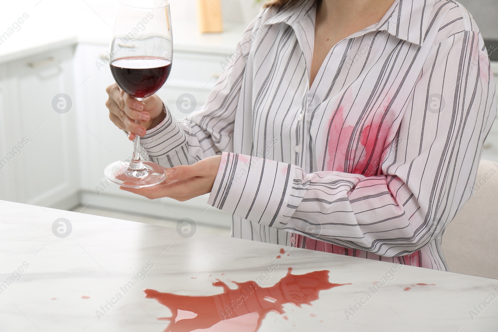 Photo of Woman with spilled wine over her shirt and marble table in kitchen, closeup