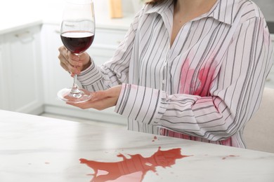 Woman with spilled wine over her shirt and marble table in kitchen, closeup