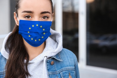 Image of Woman wearing medical mask with European Union flag, outdoors. Coronavirus outbreak in Europe
