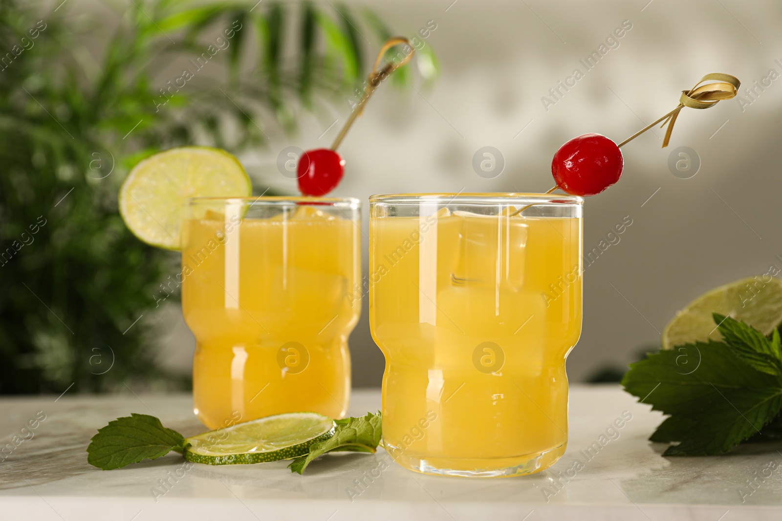 Photo of Glasses of tasty pineapple cocktail with cherry, lime and mint on white table