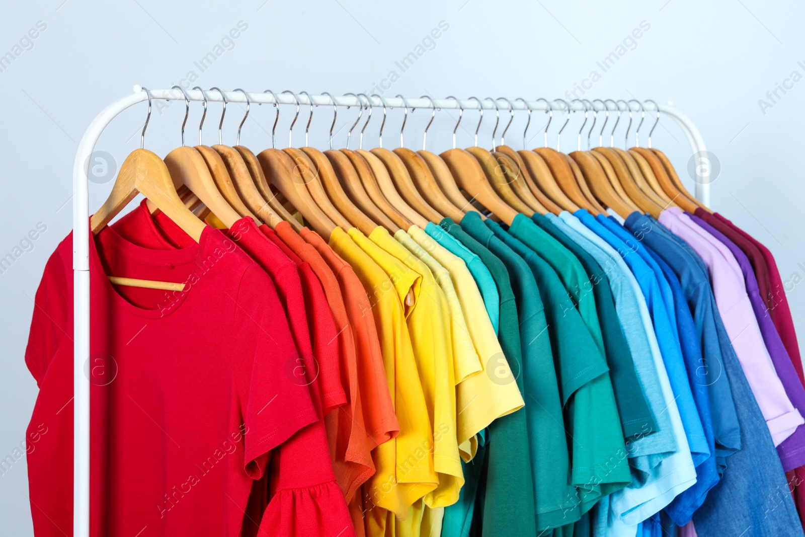 Photo of Rack with bright clothes on light blue background. Rainbow colors