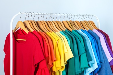 Rack with bright clothes on light blue background. Rainbow colors