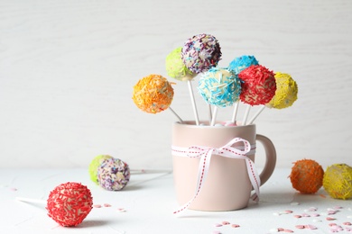 Cup with bow and yummy colorful cake pops on table. Space for text