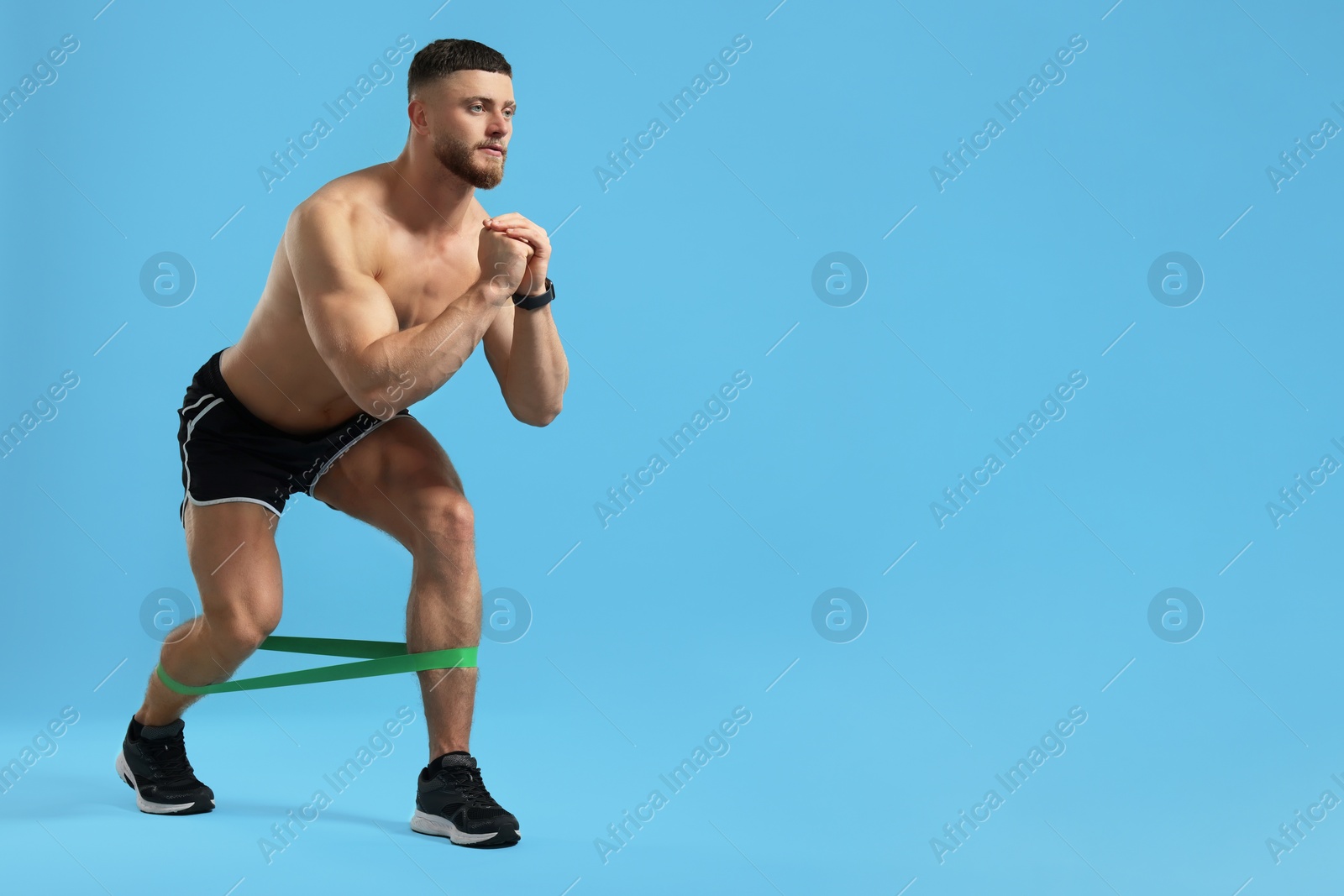 Photo of Muscular man exercising with elastic resistance band on light blue background. Space for text