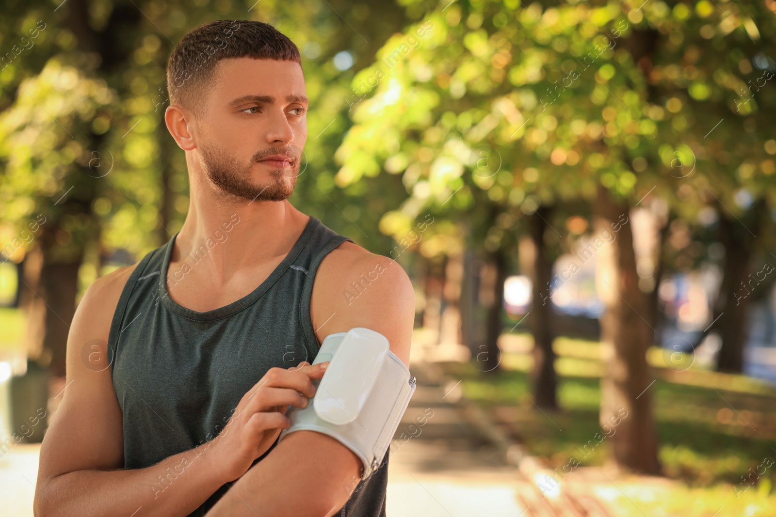 Photo of Attractive serious man checking blood pressure with modern monitor after training in park. Space for text