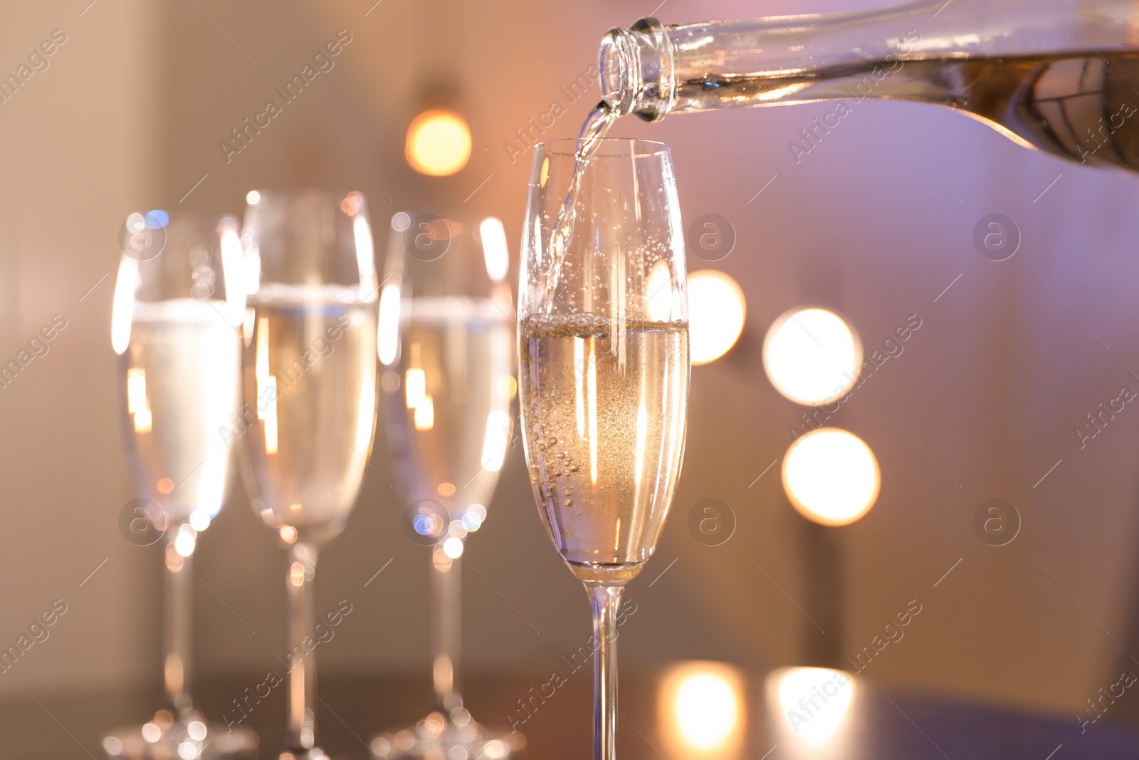 Photo of Champagne pouring from bottle into glass on blurred background, closeup. Space for text