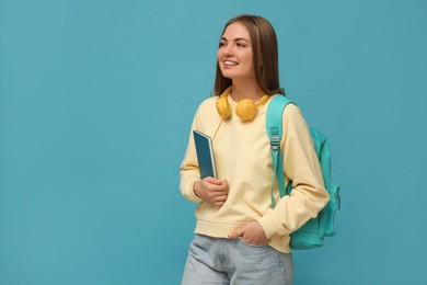 Photo of Teenage student with headphones, backpack and book on light blue background